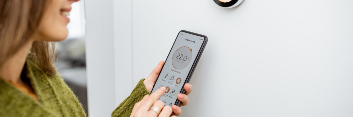 Woman regulating heating temperature with phone and thermostat at home